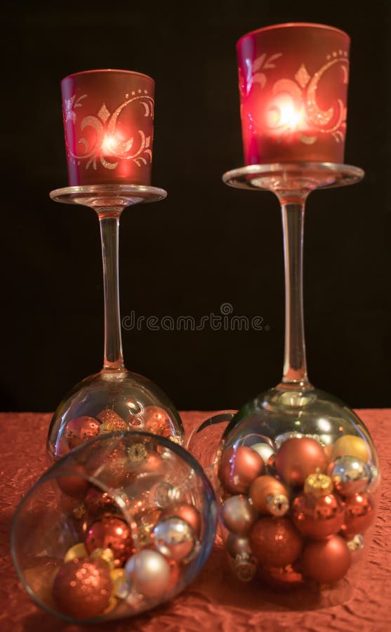 3 champagne glasses filled with colorful Christmas balls on a gray star-shaped coasters. 2 of the 3 glasses of sparkling wine are turned around and carry 2 red tea light holder with burning tea lights. 3 champagne glasses filled with colorful Christmas balls on a gray star-shaped coasters. 2 of the 3 glasses of sparkling wine are turned around and carry 2 red tea light holder with burning tea lights.