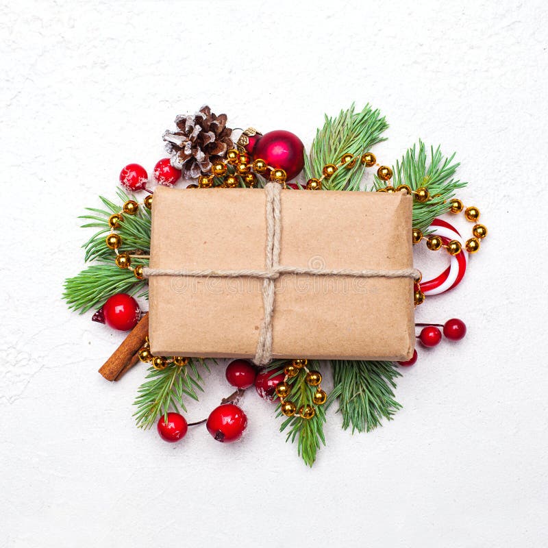 Christmas composition. Craft paper gift box, green fir twig, candy, baubles and red holly berries on white stucco plaster textured