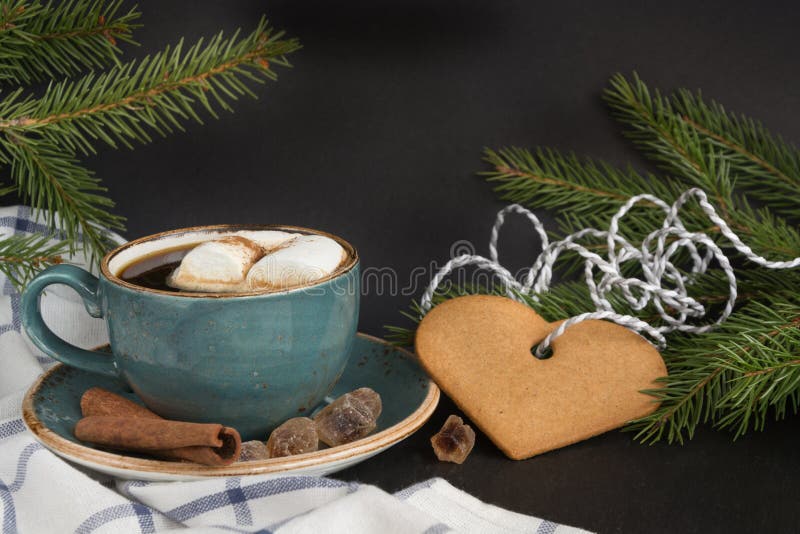 Christmas concept. Blue mug of hot coffee with marshmallow and cookies on a black background with Christmas tree branches. Close u