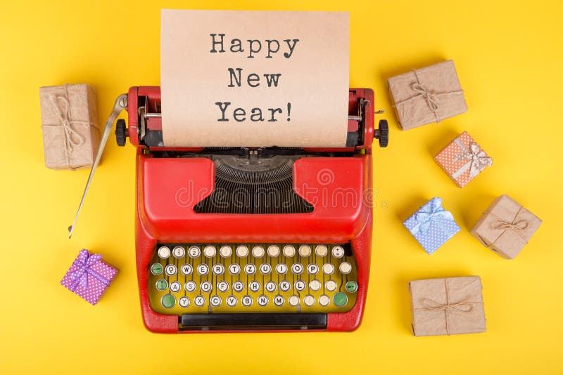 Christmas concept red typewriter with the text & x22;Happy New Year!& x22;, gift boxes and wrapping paper on yellow background