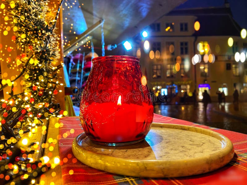 Christmas decoration and red candle red glass cup on market place kiosk top in Tallinn old town city night blurred light people wa