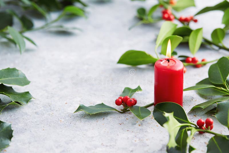 Christmas decorations, candle and holly leaves with red berries.