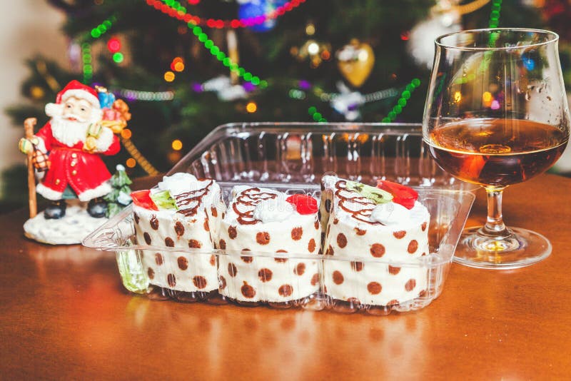 Christmas dessert set. Three mouth-watering cakes in the transparent box, brandy in elegant glass and the figure of Santa Claus in the background. Christmas dessert set. Three mouth-watering cakes in the transparent box, brandy in elegant glass and the figure of Santa Claus in the background