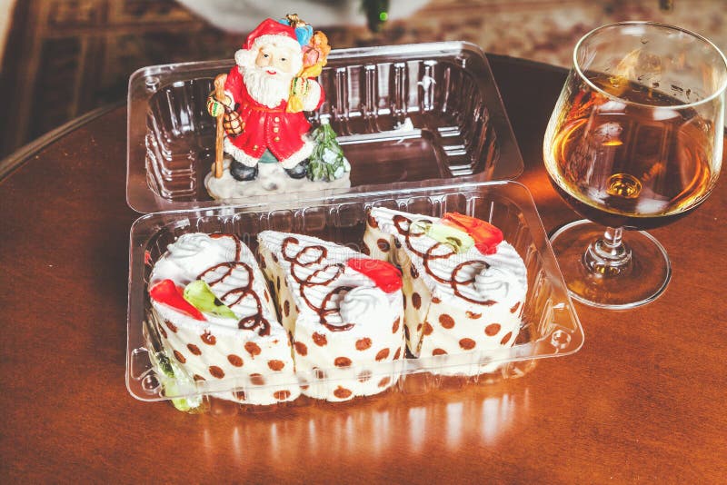 Christmas dessert set. Three mouth-watering cakes in the transparent box, brandy in elegant glass and the figure of Santa Claus in the background. Christmas dessert set. Three mouth-watering cakes in the transparent box, brandy in elegant glass and the figure of Santa Claus in the background