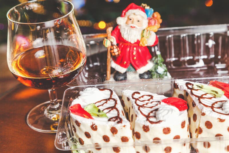 Christmas dessert set. Three mouth-watering cakes in the transparent box, brandy in elegant glass and the figure of Santa Claus in the background. Christmas dessert set. Three mouth-watering cakes in the transparent box, brandy in elegant glass and the figure of Santa Claus in the background