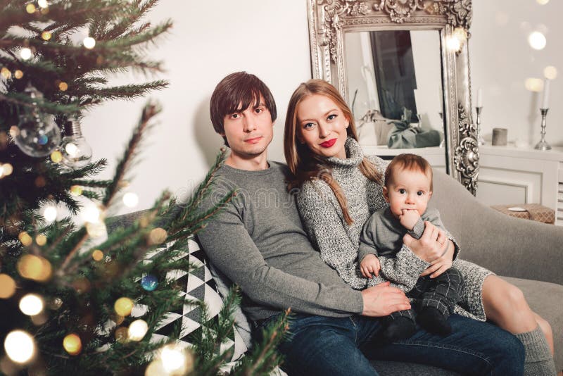 Christmas family with baby smiling near the Xmas tree. Living room decorated by Christmas tree and present gift boxes, the light royalty free stock photography Christmas family with baby smiling near the Xmas tree. Living room decorated by Christmas tree and present gift boxes, the light royalty free stock photography