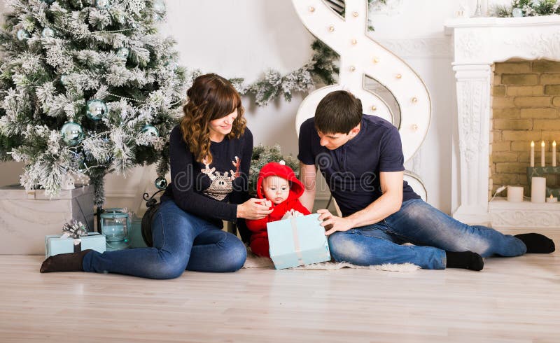 Christmas Family Open Present Gift Box, Mother Father and Baby Child in Decorated Room, sitting under Christmas Tree.
