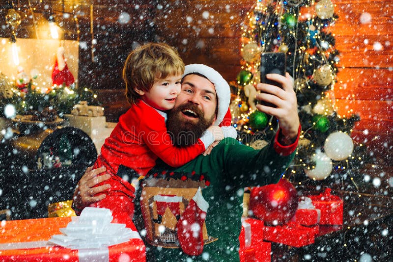 Christmas family in snow. Happy father and son talking with mobile phone near Christmas tree. Little Santa and old stock photos Christmas family in snow. Happy father and son talking with mobile phone near Christmas tree. Little Santa and old stock photos