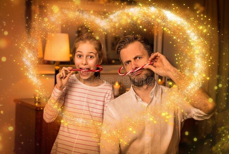 Christmas happy family time - carefree caucasian father and daughter playing clowning around while holding candy canes. Moody warm gold light, magical sparkles, cozy atmosphere at home. Christmas happy family time - carefree caucasian father and daughter playing clowning around while holding candy canes. Moody warm gold light, magical sparkles, cozy atmosphere at home.