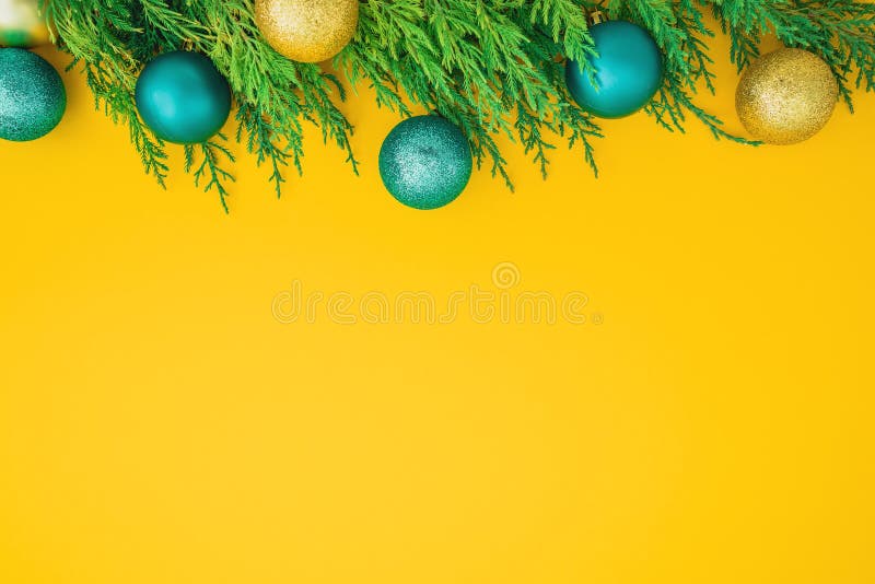 Christmas frame concept made of evergreen branches and balls decoration on yellow background. Flat lay