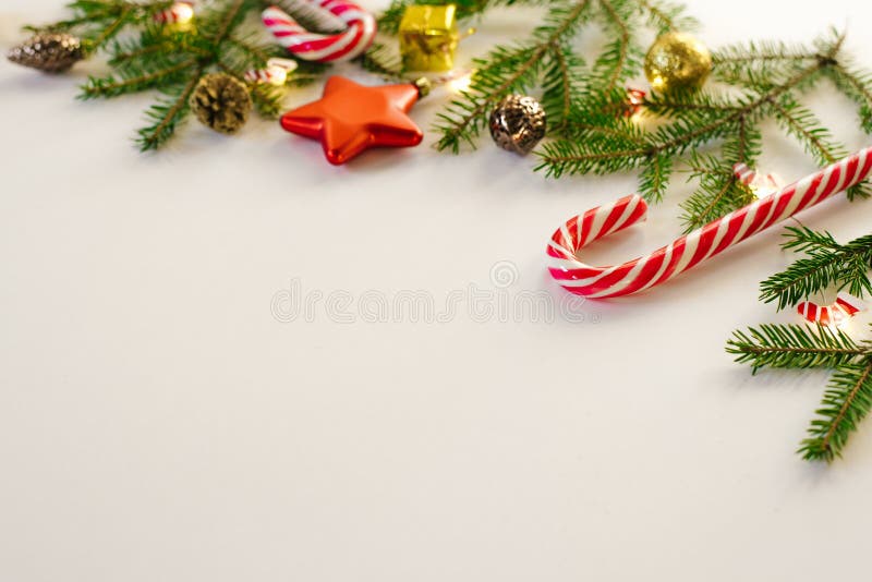 Christmas frame of fir branches and gold and brown Christmas tree toys, mint candy canes and burning lights on white background, c