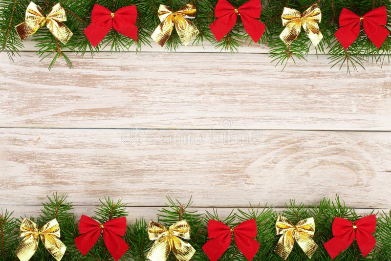 Christmas frame made of fir branches decorated with bows on a light wooden background