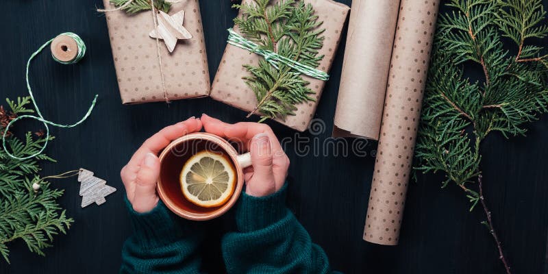 Christmas gift boxes wrapped in kraft paper. Womans hand holding cup with tea