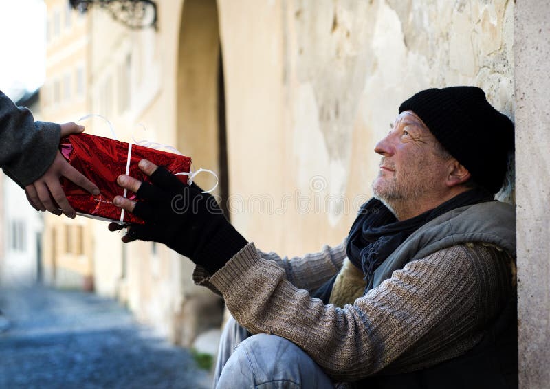 Las chicas mano es un dar regalo de navidad sobre el sin hogar hombre.