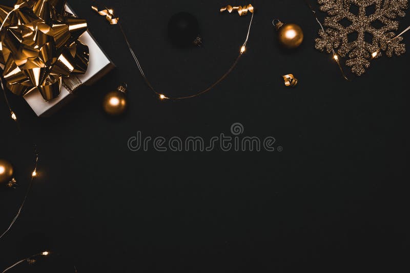 Christmas gift. White gift with golden bow, gold balls and sparkling lights garland in xmas decoration on dark background for