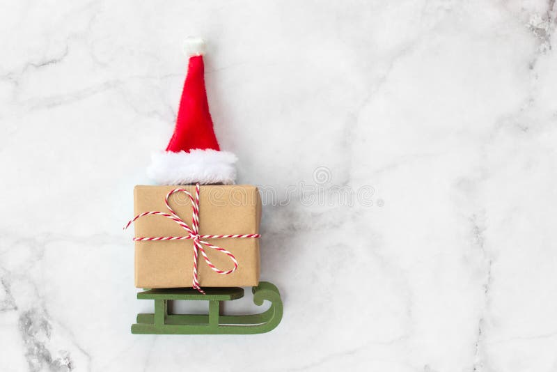Christmas gift wrapped in brown craft paper and red hat on wooden sleigh Christmas toys on gray marble background. New Year, royalty free stock image Christmas gift wrapped in brown craft paper and red hat on wooden sleigh Christmas toys on gray marble background. New Year, royalty free stock image