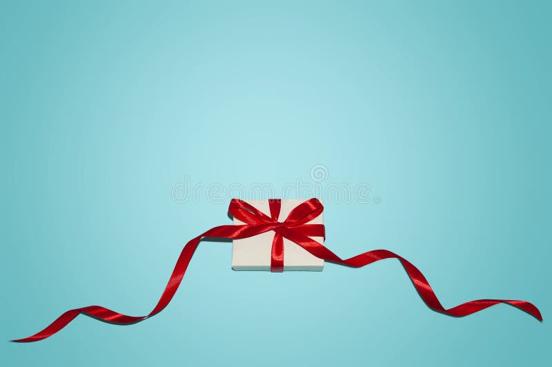 Christmas Holiday Composition. New Year Gift in White Box with Red Ribbon on Blue Background Flat Lay Top View with Copy Space royalty free stock image Christmas Holiday Composition. New Year Gift in White Box with Red Ribbon on Blue Background Flat Lay Top View with Copy Space royalty free stock image