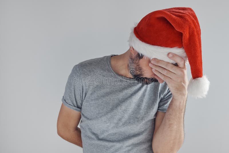 Christmas holiday depression, sad sulking man with Santa Claus hat covering face with his hands and crying alone