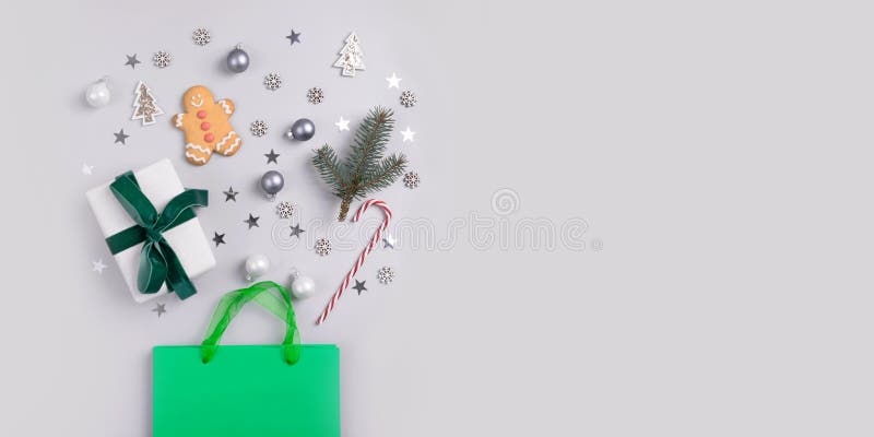 Christmas holiday shopping concept. Green bag with festive gifts, candy cane, treats, decor, glitter confetti on grey background