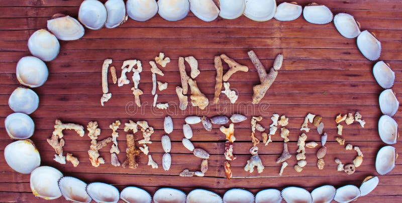 Christmas inscription from white corals and shells on wooden background.