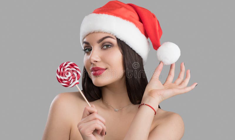 Christmas-kvinna. Snygg vintermodelltjej i tomtehatt med röda läppar och xmas lollipop-godis i hennes hand