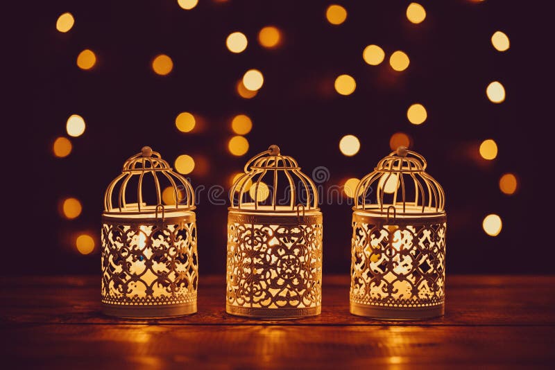 Christmas lantern with burning candles and garland on vintage wooden table with golden bokeh
