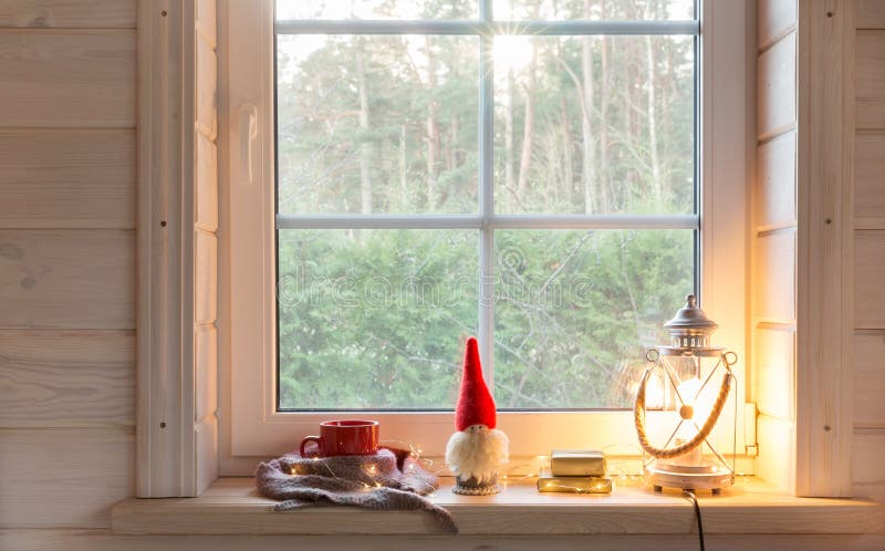 Christmas lantern, Christmas gnome,and red mug on the window of a wooden house overlooking the winter garden.