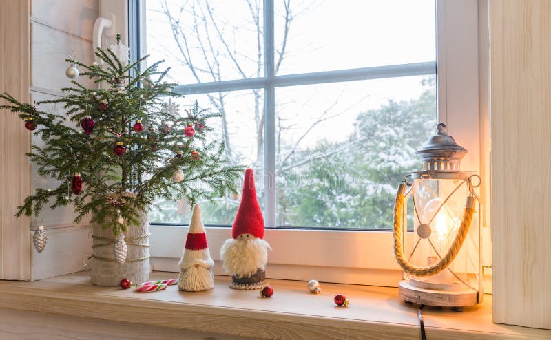 Christmas lantern, Christmas gnome, Christmas tree and red decor on the window of a wooden house overlooking the winter