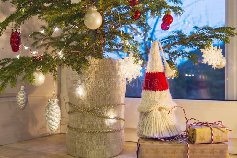 Christmas lantern, Christmas gnome, Christmas tree and red decor on the window of a wooden house overlooking the winter