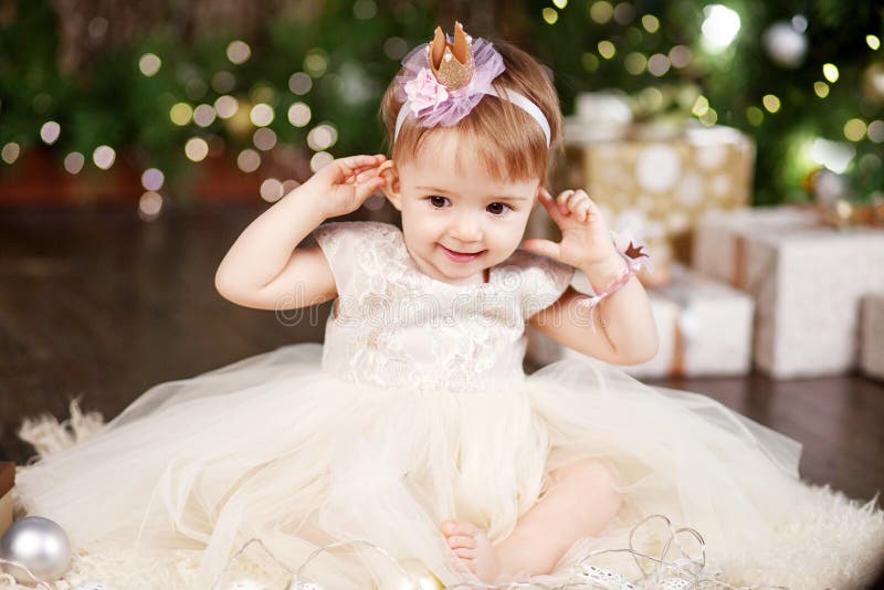 Christmas and New Year celebration concept. Pretty little girl in white dress playing and being happy about christmas tree and royalty free stock photography Christmas and New Year celebration concept. Pretty little girl in white dress playing and being happy about christmas tree and royalty free stock photography
