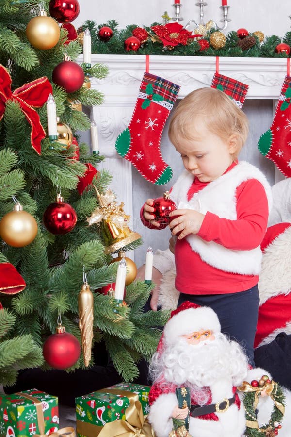 Christmas or New year celebration. Little girl in cute red jacket and a fur vest decorating Christmas tree at home near the firepl royalty free stock image Christmas or New year celebration. Little girl in cute red jacket and a fur vest decorating Christmas tree at home near the firepl royalty free stock image