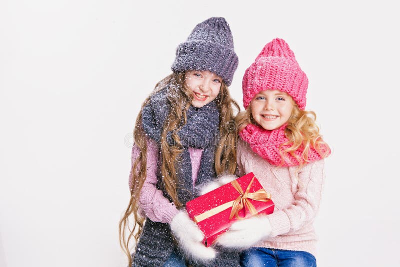 Christmas. New Year. Two little sisters holding present in winter clothes. Pink and grey hats and scarfs. Family. Winter royalty free stock image Christmas. New Year. Two little sisters holding present in winter clothes. Pink and grey hats and scarfs. Family. Winter royalty free stock image