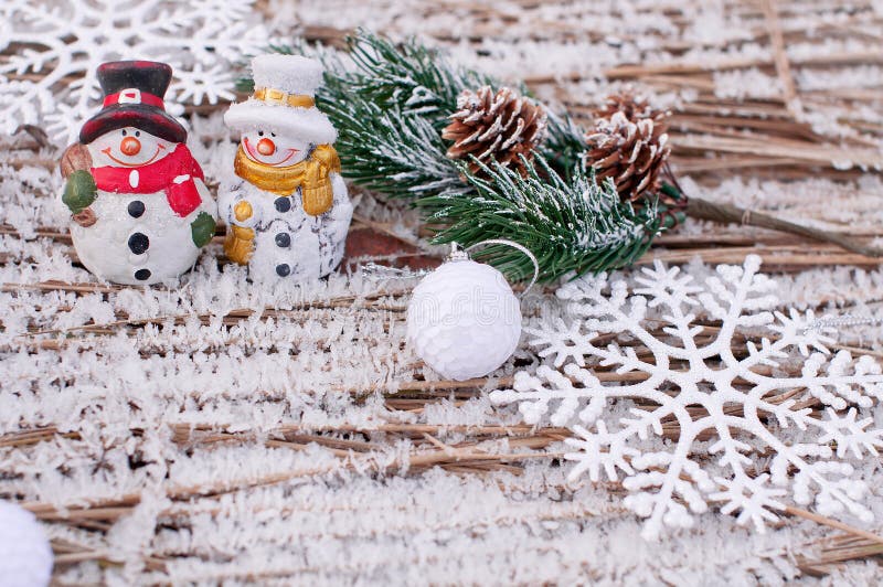 Christmas outdoor background with cheerful snowmen with colored scarves that stand on frozen grass with ice crystals and fir cones