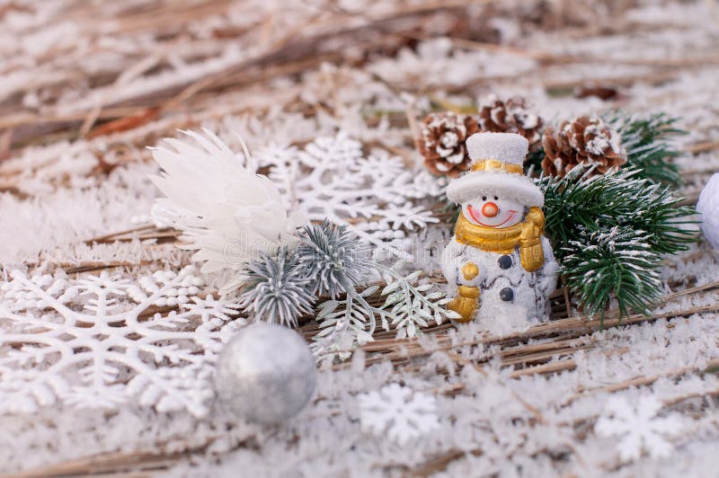 Christmas outdoor background with cheerful snowmen with colored scarves that stand on frozen grass with ice crystals and fir cones