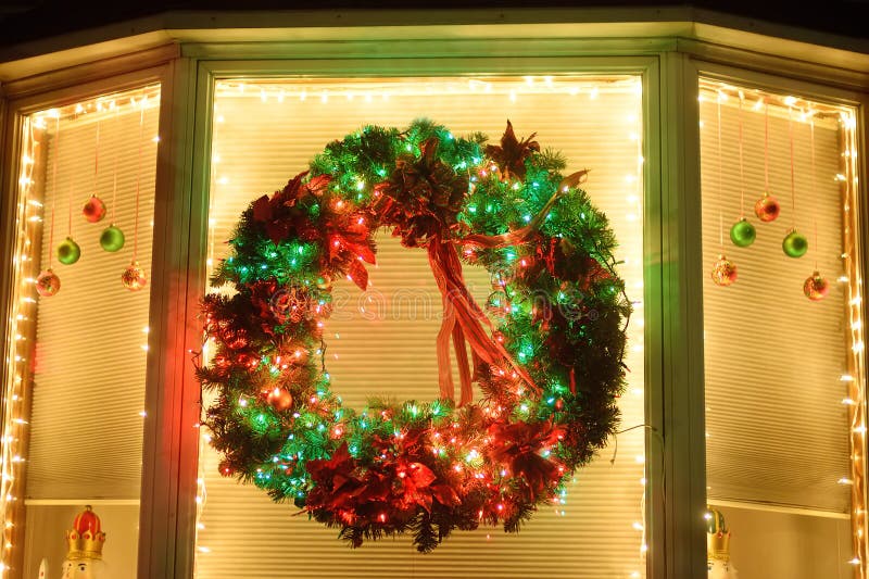 Christmas red and green wreath with ribbon on the window. Facade to the house decorated for the winter holiday - Xmas and New Year