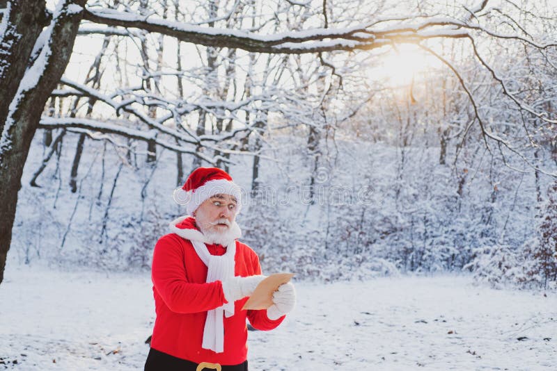 Christmas Santa reading letter near the Christmas nature background. Funny Santa in Santa hat read letter over winter
