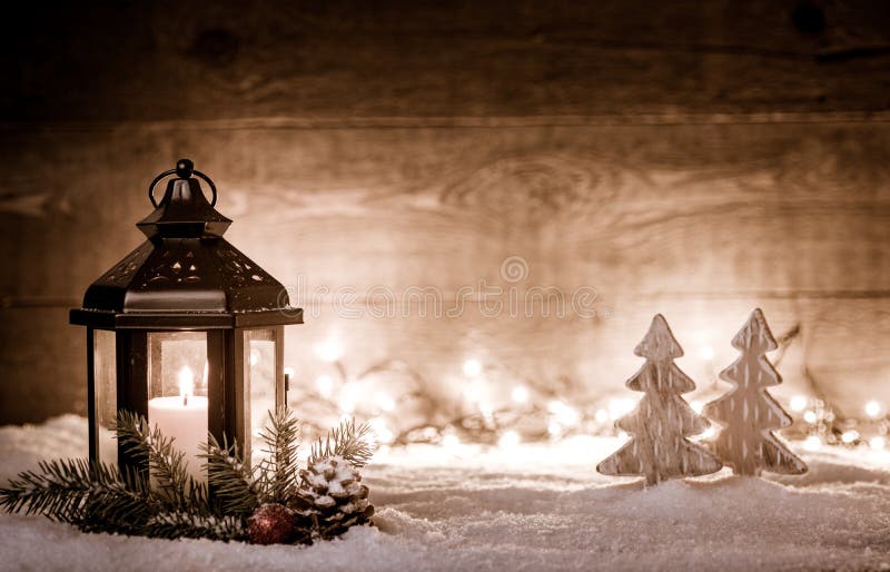 Christmas scene with a lantern, trees, fir branch, snow flakes and blurred lights in front of an illuminated dark wooden board as stock photos Christmas scene with a lantern, trees, fir branch, snow flakes and blurred lights in front of an illuminated dark wooden board as stock photos
