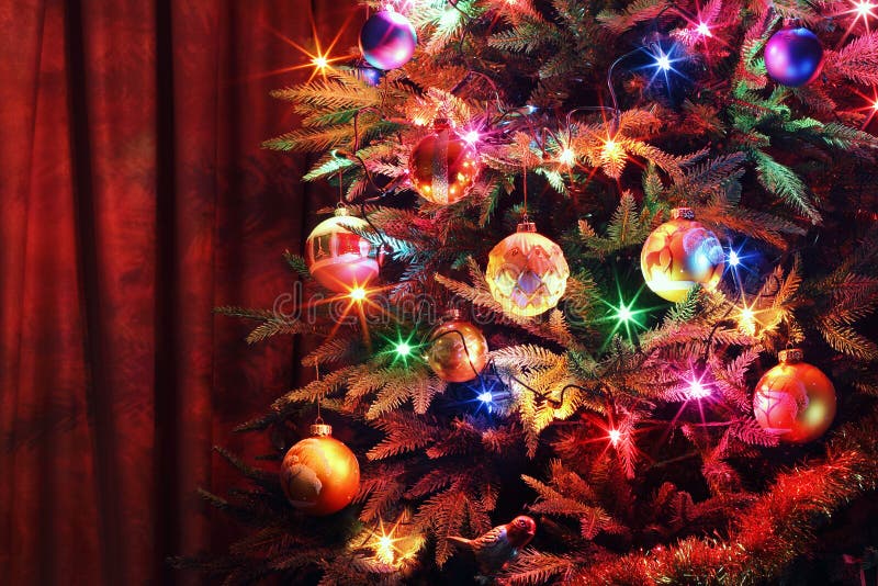 Vánoční strom s míčky, zářící girlandy a pozlátko na pozadí záclony.