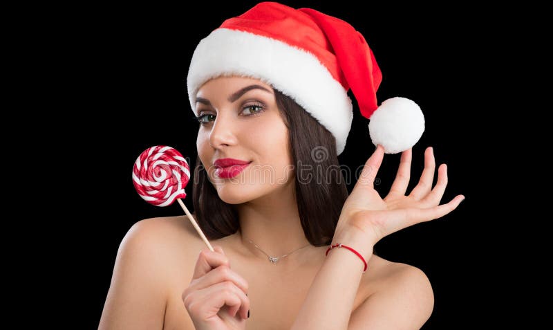Christmas woman. Beauty winter model girl in Santa Claus hat with red lips and xmas lollipop candy in her hand
