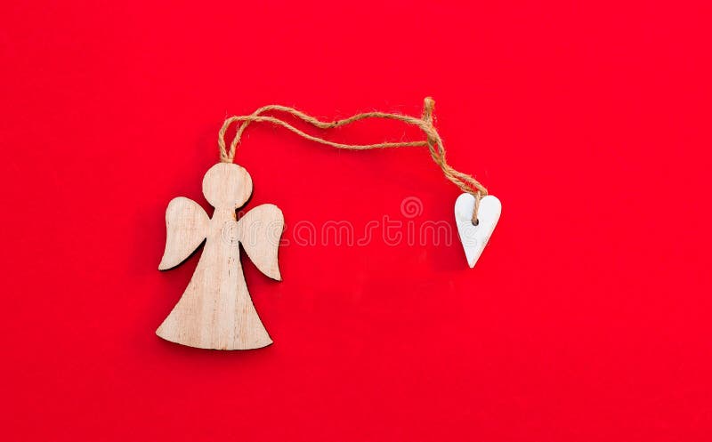 Christmas wooden angel with heart and twine on bright red background. Minimalism concept.