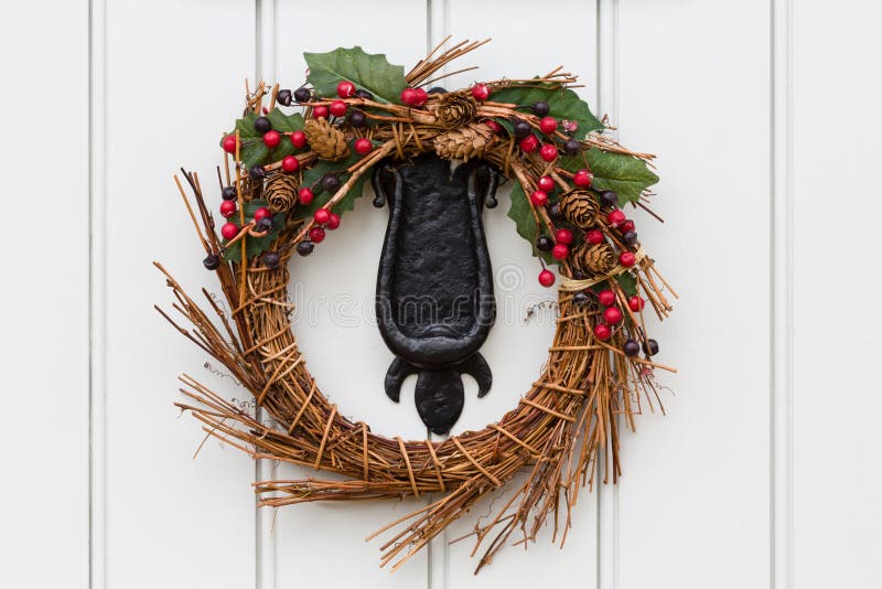 Christmas wreath on a traditional front door. Detail of a Christmas wreath or garland on the cast iron knocker of a traditional painted wooden door royalty free stock images Christmas wreath on a traditional front door. Detail of a Christmas wreath or garland on the cast iron knocker of a traditional painted wooden door royalty free stock images