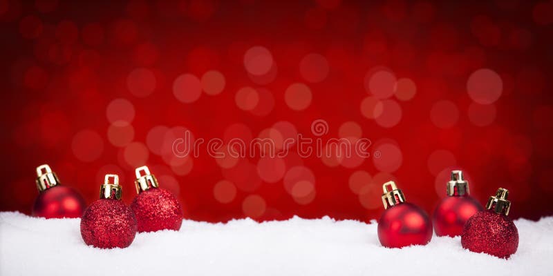 Chucherías rojas de la Navidad en nieve con un fondo rojo