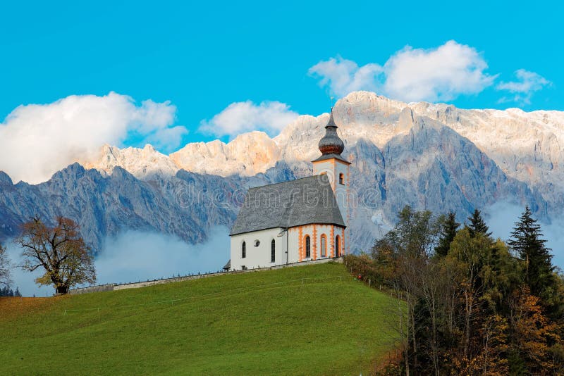 A church standing high on the grassy hilltop with a rocky mountain range in the background