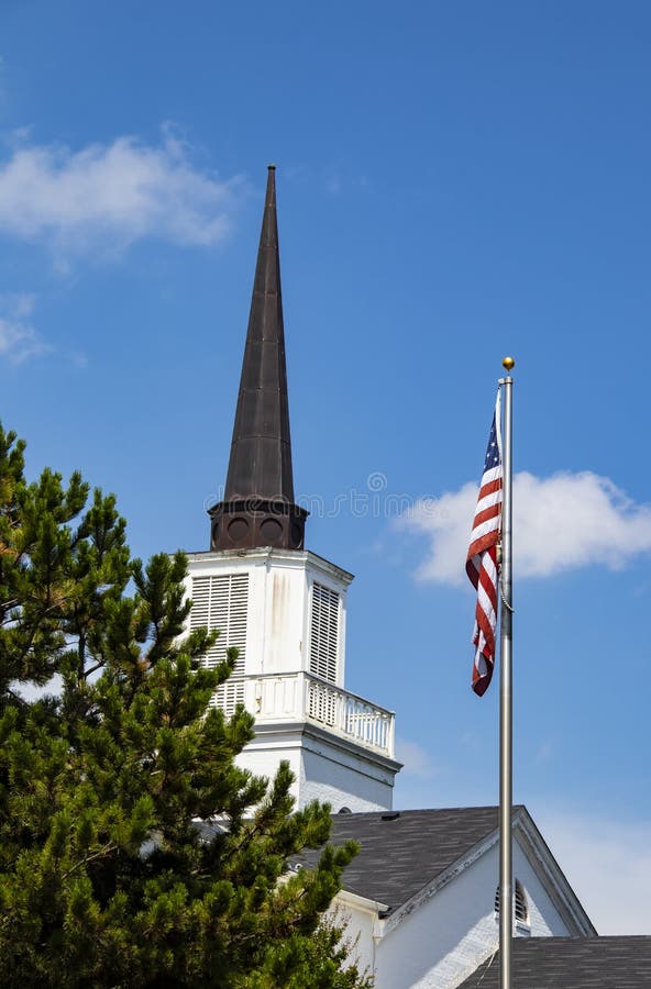Church and state - Church spire and American flag with evergreen tree and blue sky with clouds