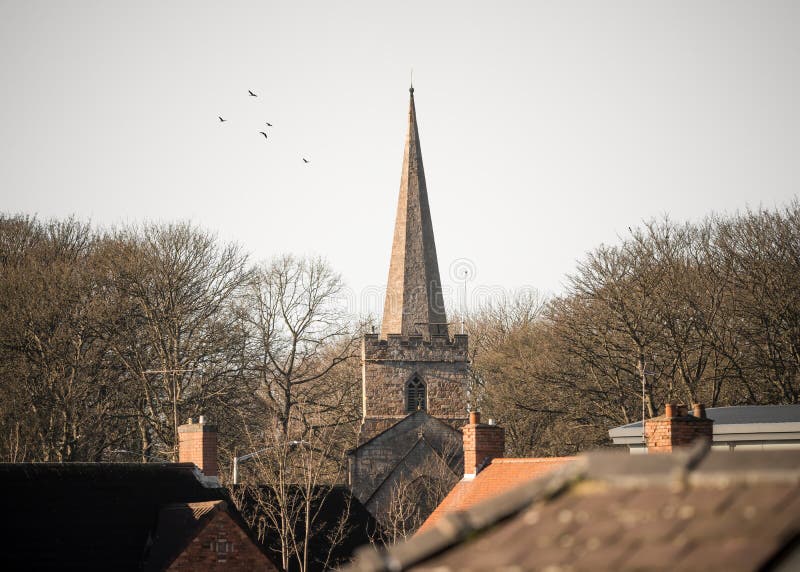 Church stone pointed spire in village centre rising above residential houses