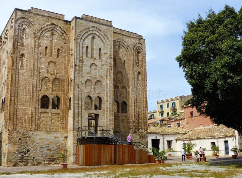 Castle of Cuba of the Norman kings of Sicily. Palermo. Sicily. Travel destination. Blue clear sky. Sunny day. Springtime and holidaytime. Arabic norman style. Rectangular shape. Arch windows. Ochre color. People. Ancient and old building around. Vases of plants. Tree and dry grass. Iron staiways. Castle of Cuba of the Norman kings of Sicily. Palermo. Sicily. Travel destination. Blue clear sky. Sunny day. Springtime and holidaytime. Arabic norman style. Rectangular shape. Arch windows. Ochre color. People. Ancient and old building around. Vases of plants. Tree and dry grass. Iron staiways.