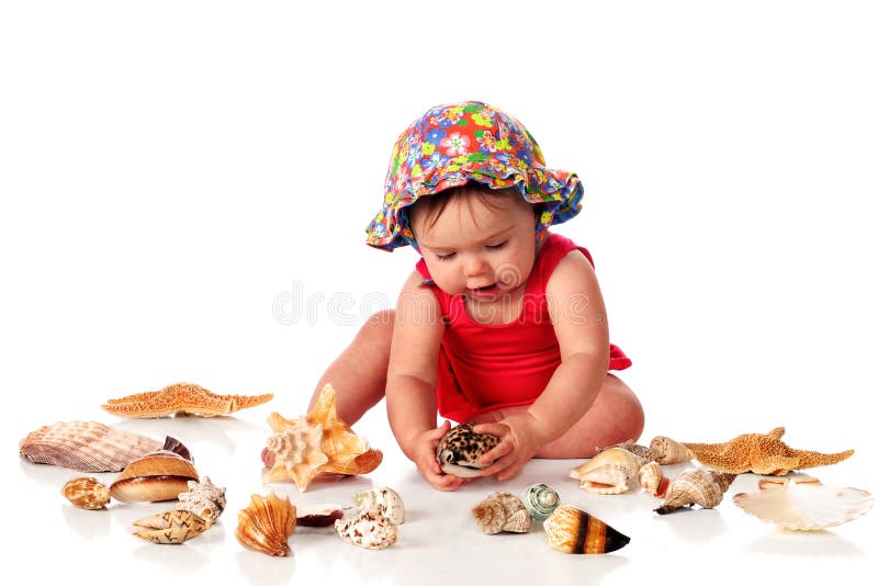 An adorable baby girl in her swimsuit and sunhat examining one of several seashells. Isolated on white. An adorable baby girl in her swimsuit and sunhat examining one of several seashells. Isolated on white.