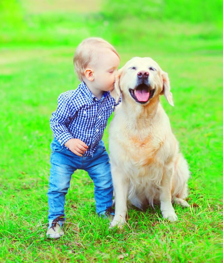 Chłopiec dziecko całuje golden retriever psa na trawie w parku fotografia stock