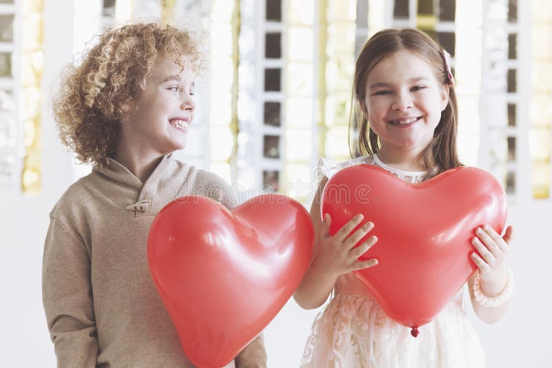 Small boy and girl holding red balloon hearts. Small boy and girl holding red balloon hearts