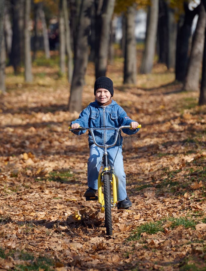 Chłopiec jazda na bicyklu w jesień parku, jaskrawy słoneczny dzień, spadać liście na tle obrazy stock Chłopiec jazda na bicyklu w jesień parku, jaskrawy słoneczny dzień, spadać liście na tle obrazy stock